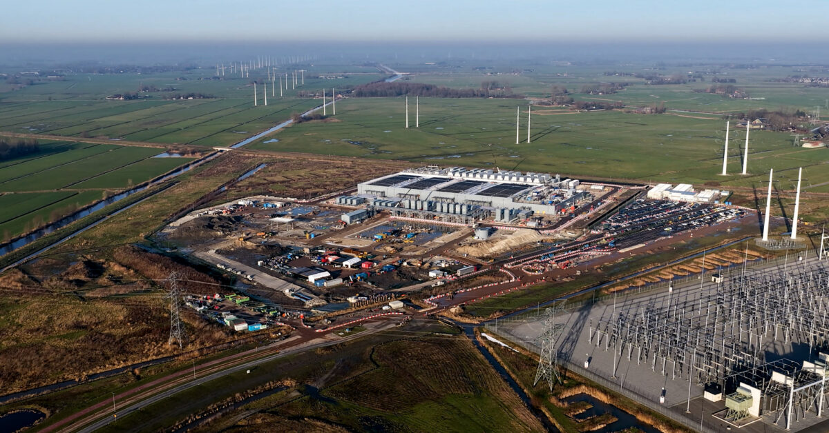Aerial view of a large construction site beside an electrical substation, transmission lines and drainage channels.